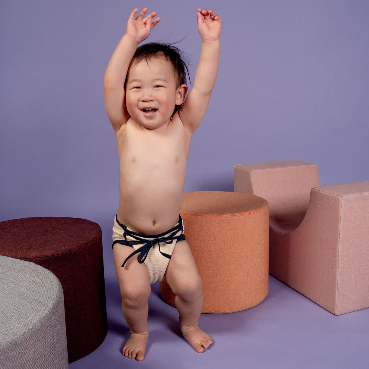 Fröhliches Kleinkind trägt weiche SUMO Stoffwindel und hebt Arme vor Freude – nachhaltiges Wickeln, das Spaß macht und gut aussieht. Foto: Briony Ridley